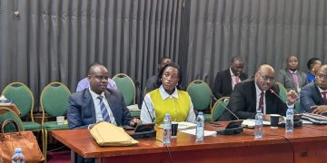 150 Local Government Officials Flagged Over Alleged Mismanagement, 40 Taken To Court KAMPALA – At least 150 local government officials have been flagged over alleged mismanagement, corruption and misuse of public resources, with 40 already facing prosecution before the Anti-Corruption Court. The Minister of Local Government, Balaam Barugahara Ateenyi, disclosed the figures while appearing before Parliament’s Public Accounts Committee (Local Governments), chaired by Mukono Municipality MP Betty Nambooze. Barugahara said nine additional case files are ready for submission to court, while 24 files are still being completed and 30 others remain under investigation. He said the figures do not include cases from West Nile and Budaka. According to the Minister, the cases were uncovered during field inspections in various local governments, where officials found alleged misuse of public funds, poorly executed projects and failures in supervision. Among the cases cited was a Shs73 million pit latrine project in Mulambuli, which Barugahara said was commissioned despite lacking a proper pit. He also cited a road project where laboratory tests allegedly found no suitable murram material, despite funds having already been spent on the works. Barugahara described some of the cases as evidence of syndicated corruption, in which several officials within local government structures allegedly fail to exercise their oversight responsibilities. “We should show these people that we know what you are doing, and it shall come for you,” Barugahara told the committee, warning that the government would take a tougher stance against officials involved in corruption and mismanagement. He further disclosed that investigations into financial irregularities had so far identified activities worth about Shs9.32 billion, with another Shs10 billion linked to a separate district. He said a forensic audit is being conducted to establish the actual amount involved through physical verification of roads and other government projects. PDM Funds Under Scrutiny The committee also raised concerns over alleged corruption and mismanagement in the implementation of the Parish Development Model (PDM), citing findings contained in the Auditor General’s reports. The audit identified cases in which some beneficiaries allegedly received PDM funds more than once, while others failed to procure the required assets. The committee also cited cases involving non-existent projects and the diversion of PDM funds to activities that were not eligible for financing under the programme. Nambooze said the scale of local government operations makes it impossible for the Minister to personally supervise every district, placing greater responsibility on the Ministry’s technical leadership. She urged the Ministry to ensure that officials implicated in corruption are thoroughly investigated and, where evidence supports the allegations, prosecuted. Nambooze warned against relying solely on interdictions, saying officials can eventually return to their positions if investigations are not concluded. She also questioned why reports from District Public Accounts Committees do not consistently reach Parliament, saying this limits lawmakers’ ability to obtain a comprehensive picture of accountability failures in local governments. MPs Asked To Strengthen Oversight Minister of State for Local Government Justine Nameere called on MPs to strengthen oversight of government projects in their constituencies by regularly visiting project sites and demanding accountability from implementers. Nameere pointed to differences in the quality and cost of government-funded construction projects as evidence of weak supervision. She cited a three-storey structure in Namagunga that she said was constructed at a cost of about Shs900 million, contrasting it with another project where only a slab and a few pillars had been completed despite substantial expenditure. She said closer monitoring by elected leaders could help expose poor workmanship, inflated costs and other forms of mismanagement before public funds are lost. Nameere also raised concerns over alleged corruption within District Service Commissions, saying some job seekers have reportedly been asked to pay money in exchange for government employment. She said some families have sold property in an attempt to secure jobs for their children, only to lose their money without the promised employment. Calls For Institutional Reform Permanent Secretary in the Ministry of Local Government Ben Kumumanya said accountability failures should not be attributed to a single individual because several institutions and officials have legally mandated responsibilities. He said the Ministry needs to review the existing accountability system, restructure ineffective structures and strengthen institutions responsible for inspection, auditing and oversight. “The time for restructuring, the time for policy reform, the time for reform is now,” Kumumanya said. The committee also questioned the independence of District Public Accounts Committees. Vice Chairperson Abed Nasser Mudiobole argued that allowing district councils to appoint committees that later scrutinise the councils’ performance creates a potential conflict of interest. He proposed amendments to the Local Government Act to strengthen the independence of the committees, including a proposal for the losing political side in LC5 elections to nominate members. Staffing Gaps Hamper Oversight The committee further raised concerns over understaffing, particularly in critical positions such as internal auditors and engineers. Nambooze said some local governments have critically low staffing levels. She cited Mukono Municipality, where she said only about five percent of the required civil servants are in place and one engineer serves the municipality and its two divisions. The Ministry, however, said staffing levels across local governments have improved from 60 percent in June 2022 to 70 percent by June 2026. Staffing at the Ministry’s headquarters currently stands at 91 percent, according to officials. The Ministry said it will continue recruiting for critical positions, strengthen inspections, improve follow-up on audit and parliamentary recommendations, enhance records management and intensify risk-based supervision. Barugahara also called for stronger coordination between central government ministries and local governments, particularly for projects contracted by central government agencies but implemented in districts. He said local government engineers should be involved in supervising such projects to ensure value for money and prevent central government agencies from shifting responsibility to districts when projects fail. Barugahara said the government would continue working with Parliament and other oversight institutions to address corruption, recover misappropriated public resources and improve service delivery. The committee, meanwhile, urged the Ministry to ensure investigations are concluded and officials found culpable are prosecuted, stressing that accountability should go beyond interdictions to include prosecution and recovery of public funds.